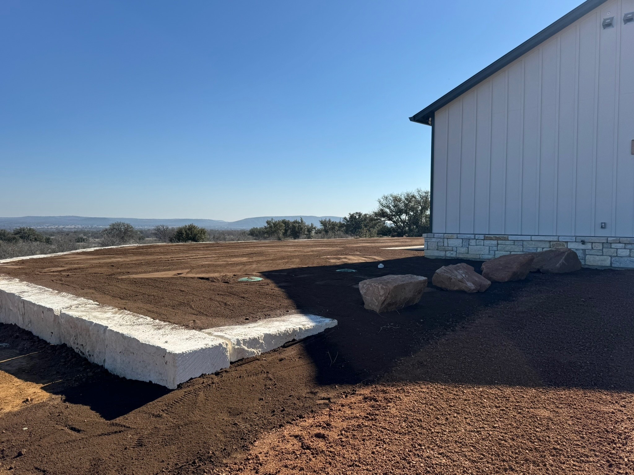 Site preparation with limestone curbing and boulders beside metal building